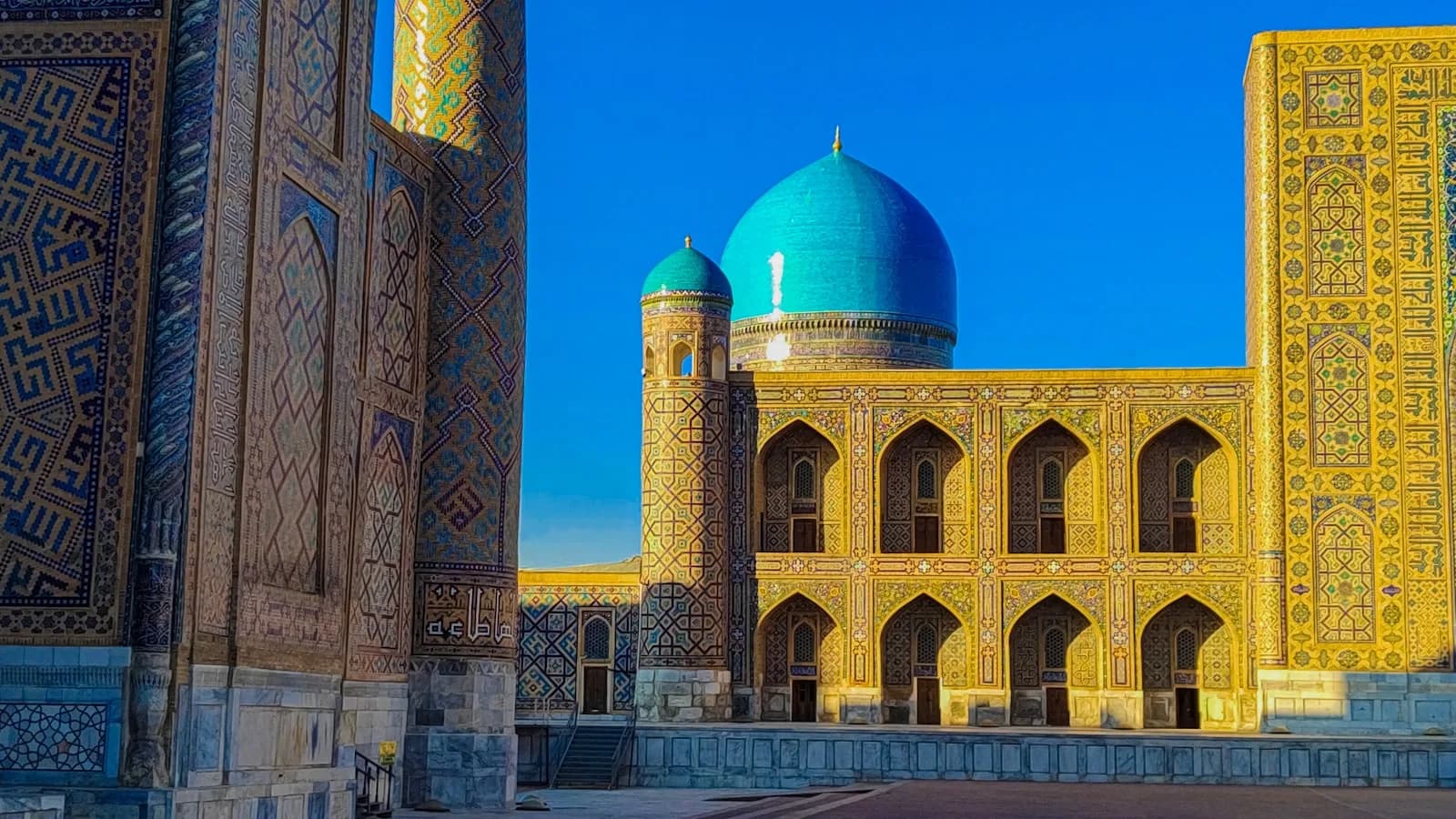 The Registan in Samarkand, Uzbekistan, its turquoise dome and gold-tiled madrasah lit by low sun against a deep blue sky | BudgetBro