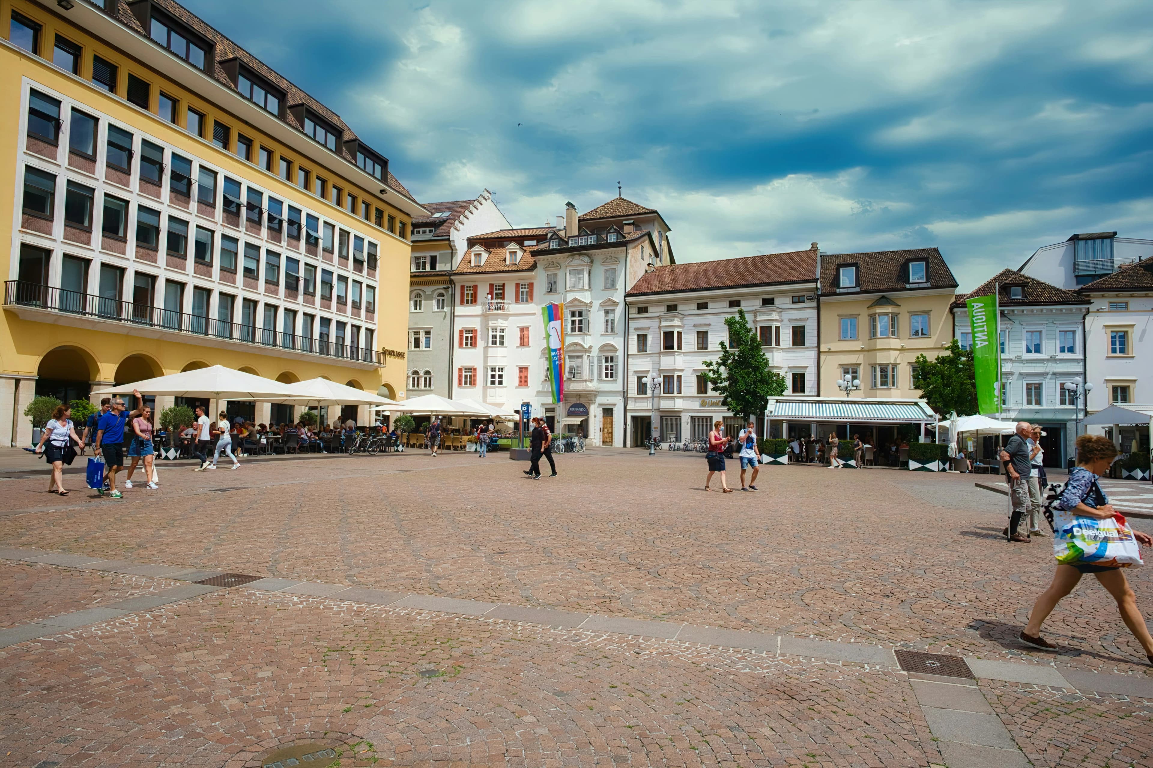Travellers walking across a sunny European town square lined with cafes, a typical day trip destination | BudgetBro
