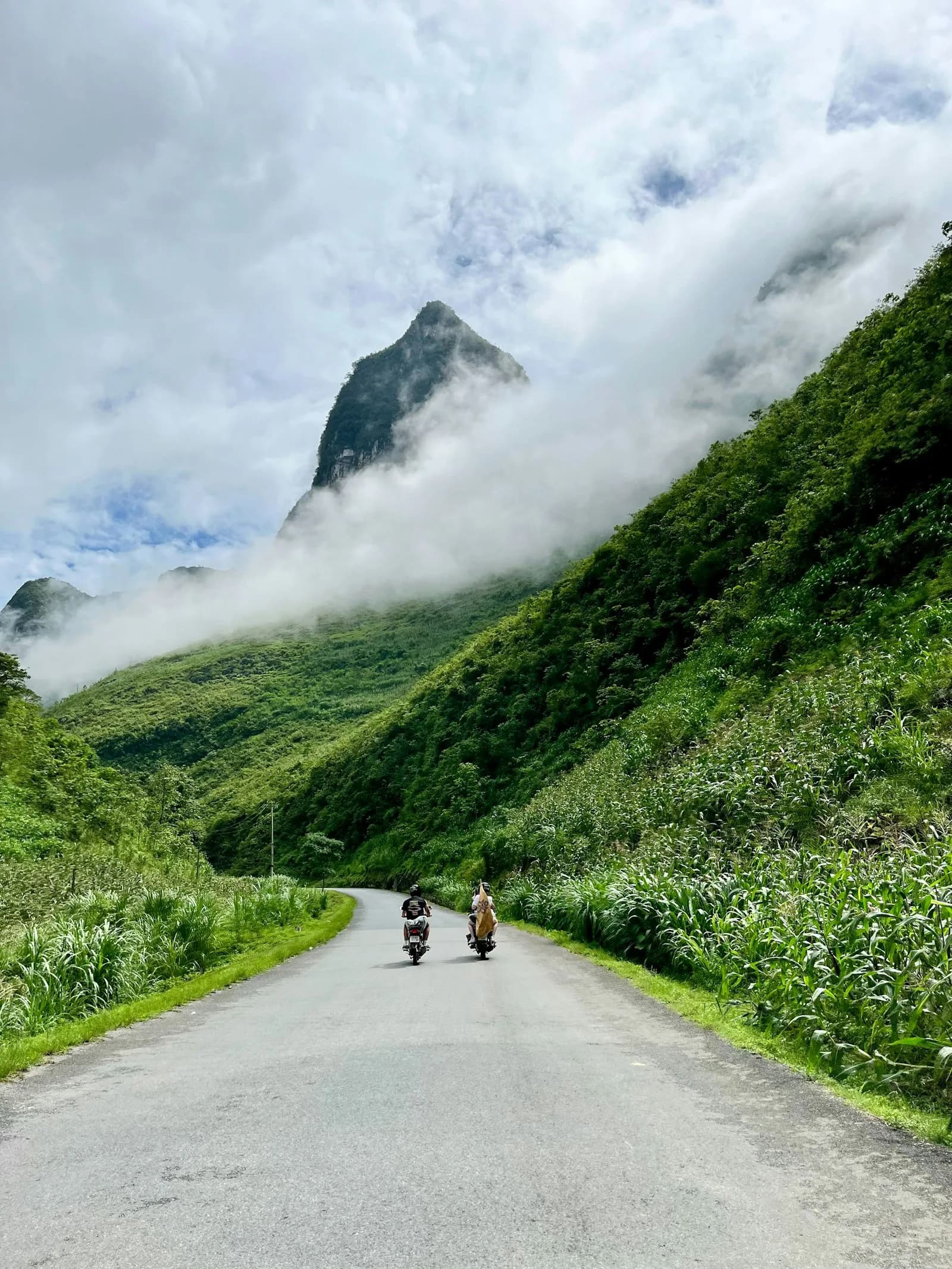 Two motorbike riders on a quiet road below misty limestone peaks on the Ha Giang Loop near the Chinese border | BudgetBro