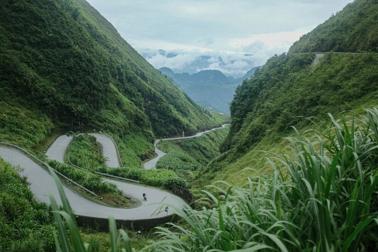 A winding switchback road descending through the green mountains of the Ha Giang Loop in northern Vietnam | BudgetBro