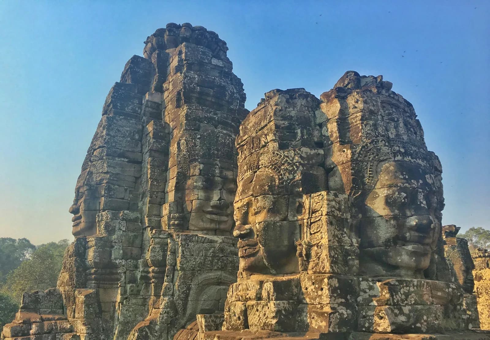 The carved stone faces of Bayon temple at Angkor Thom in Siem Reap, Cambodia, under a clear blue sky | BudgetBro