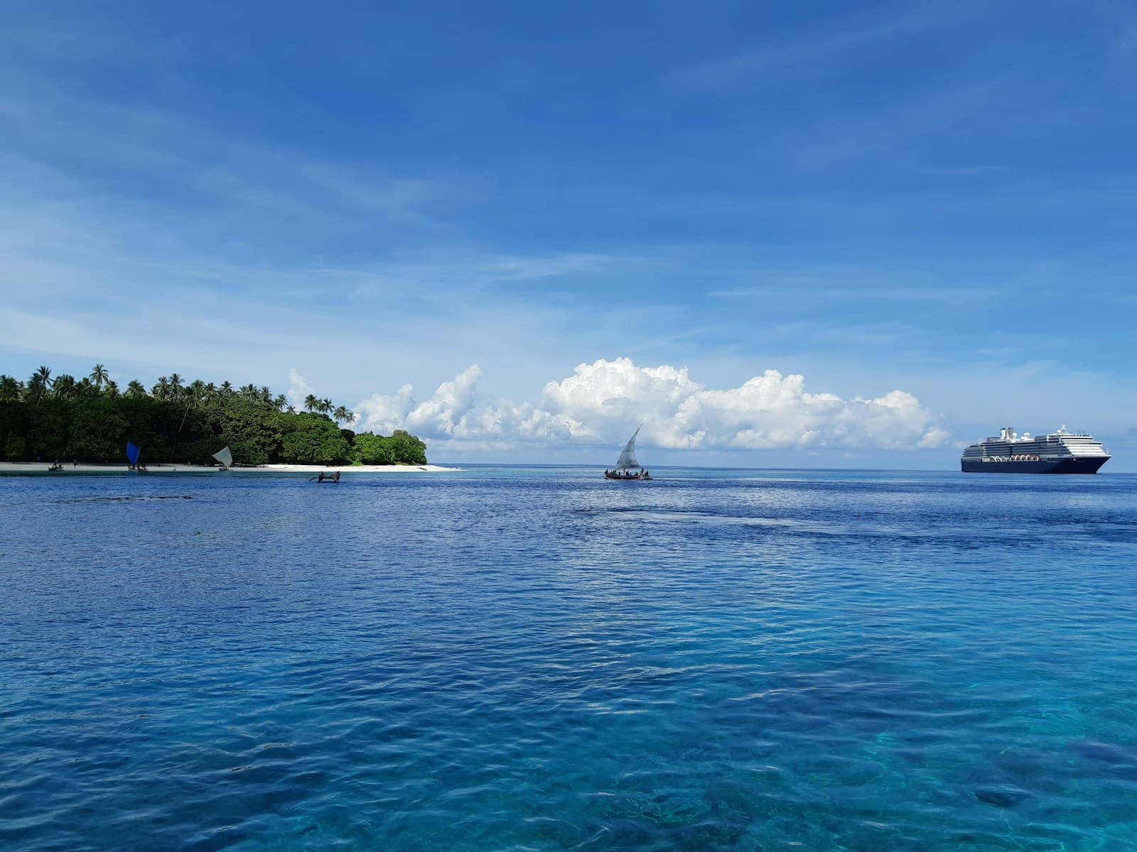 A remote green island in Papua New Guinea ringed by clear turquoise water, with a small sailing canoe offshore