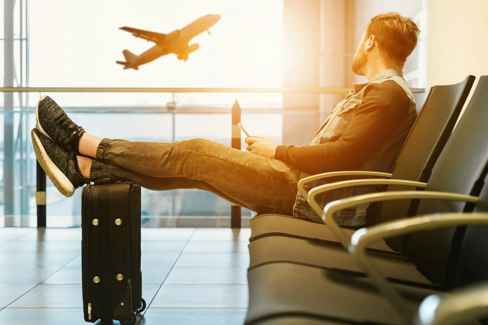 A traveller relaxing in an airport departure lounge using a smartphone as a plane takes off | BudgetBro