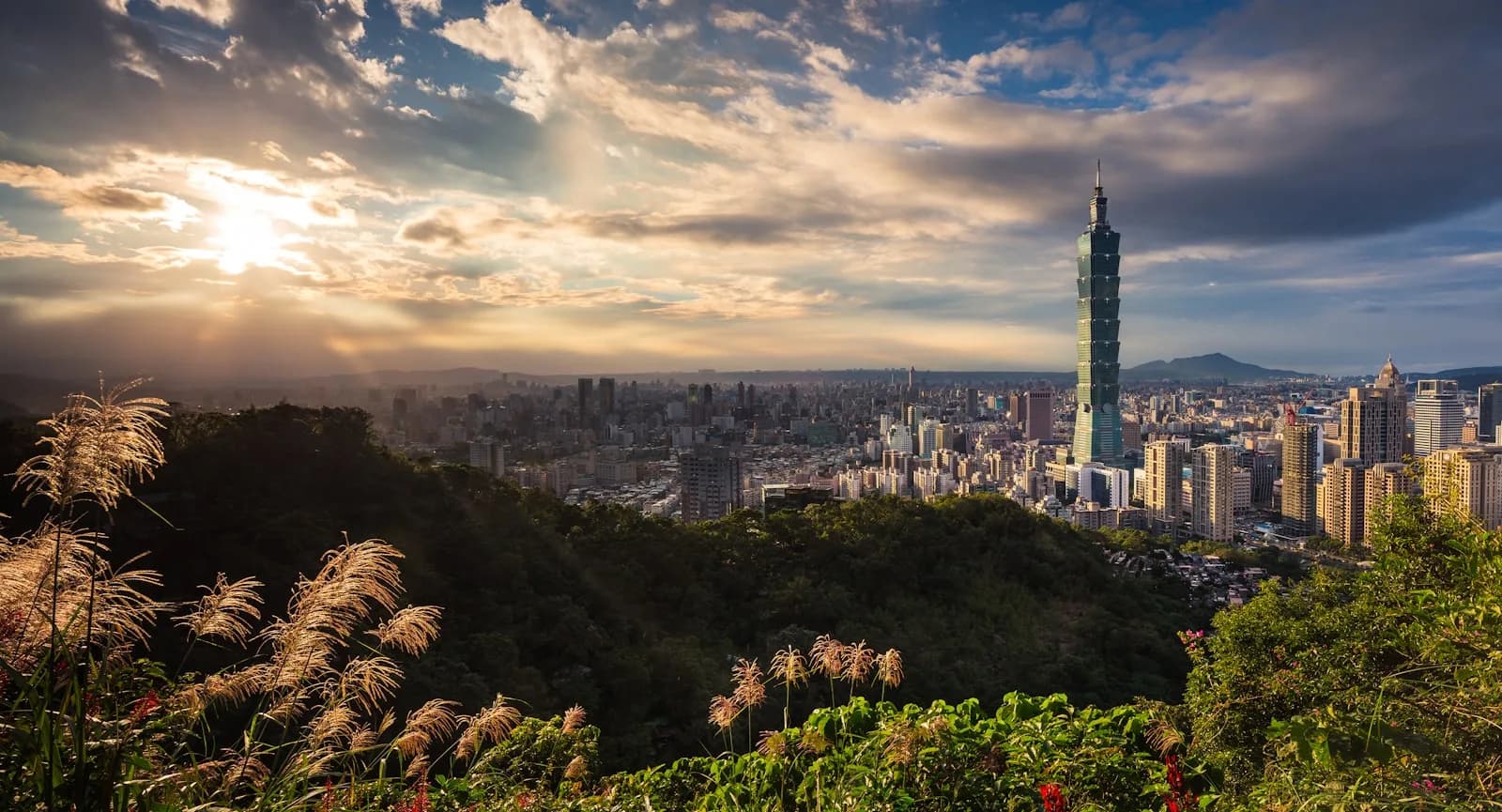 The Taipei skyline at golden hour with Taipei 101 rising above the city, seen from a green hillside in Taiwan | BudgetBro