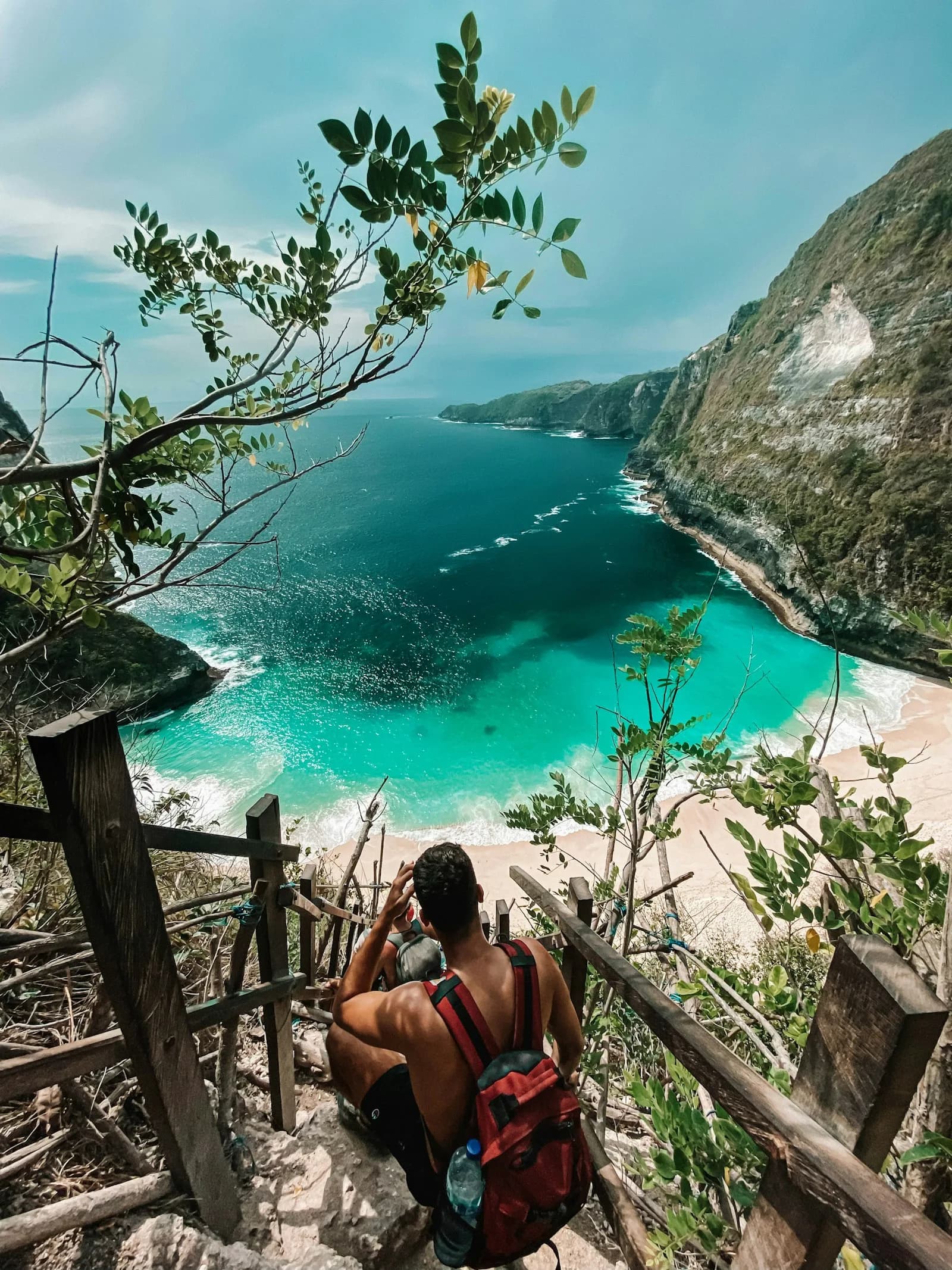 A backpacker looking down over the turquoise water of Kelingking Beach on Nusa Penida, Bali, Indonesia | BudgetBro