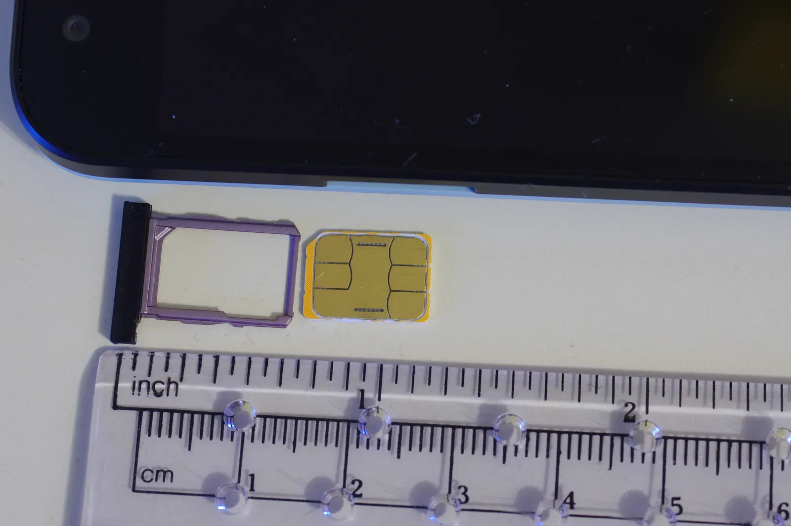 A nano SIM card next to its tray from a phone, laid on a ruler | BudgetBro