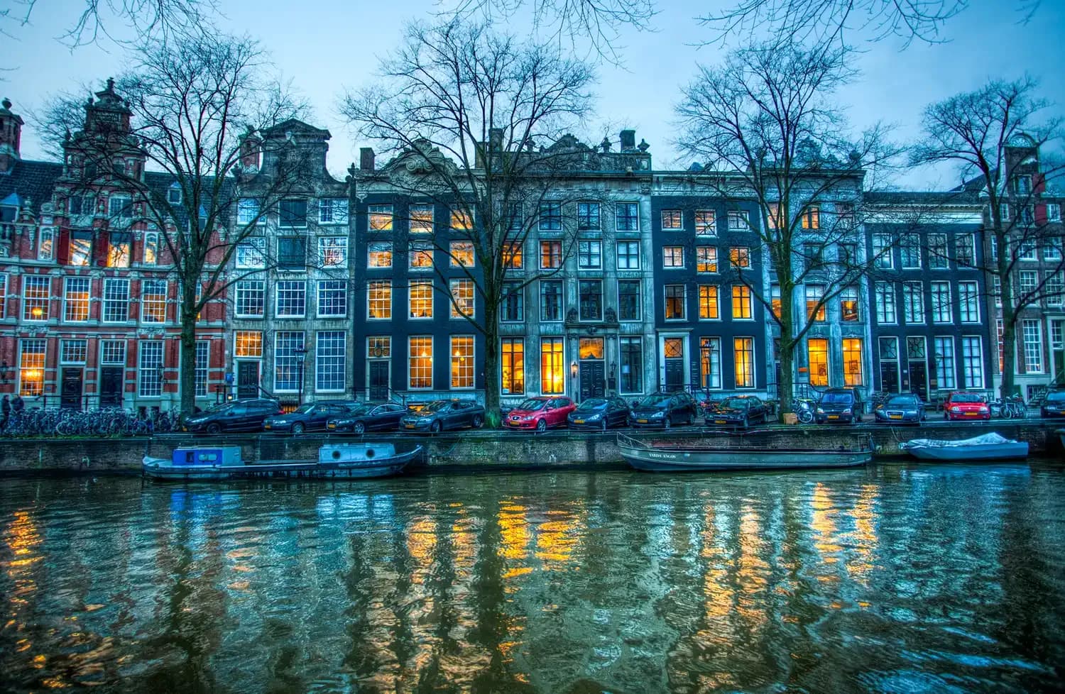 Herengracht canal houses in Amsterdam at blue hour, lights reflected in the water | BudgetBro
