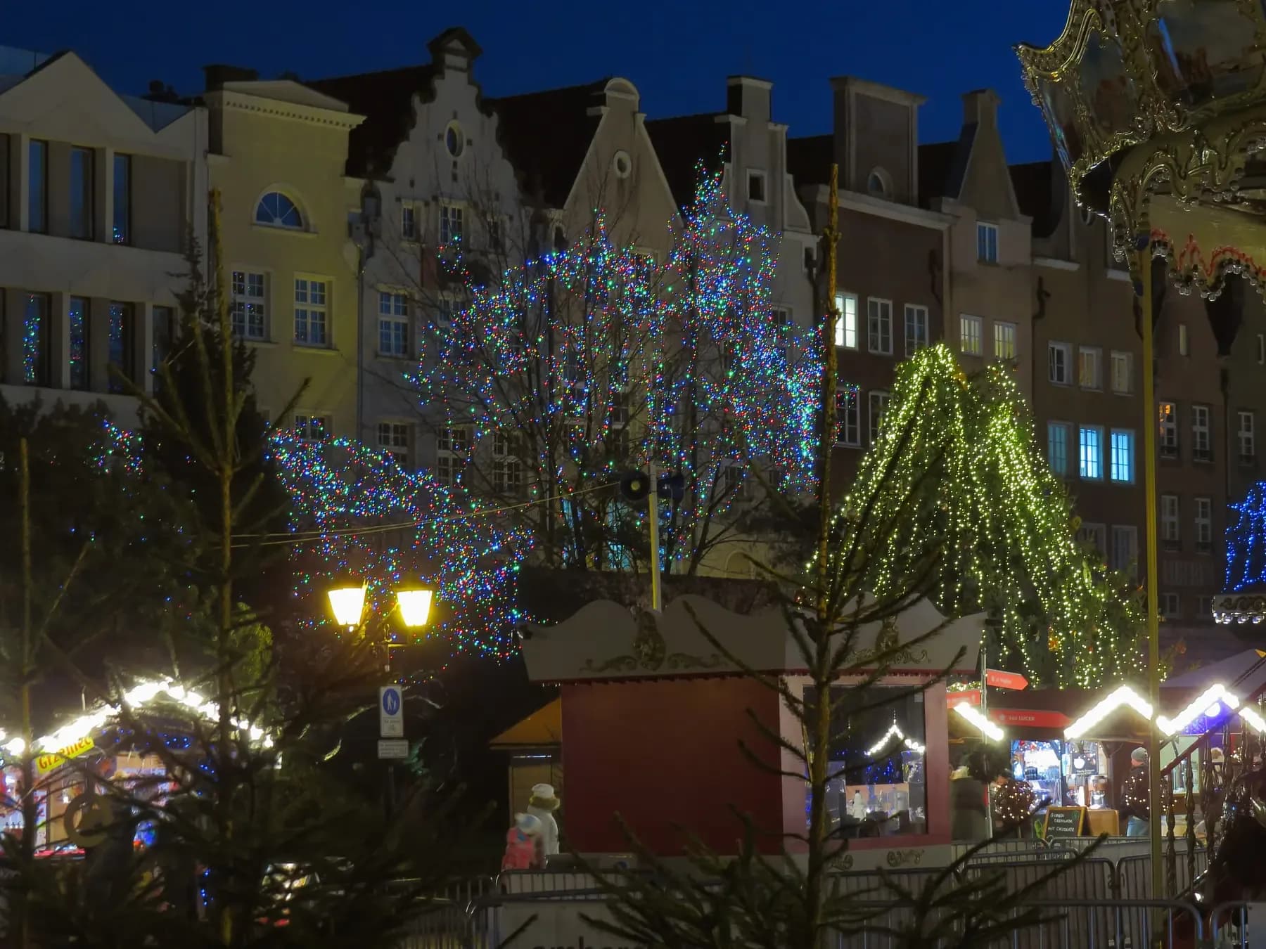 Old Town houses and trees covered in Christmas lights above market stalls in Gdańsk at dusk | BudgetBro