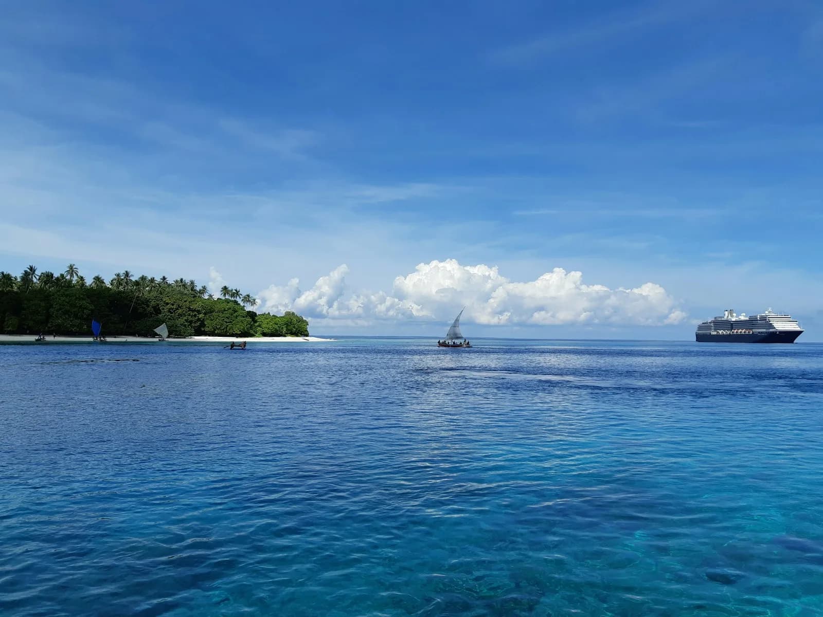 A remote green island in Papua New Guinea ringed by clear turquoise water, with a small sailing canoe offshore | BudgetBro