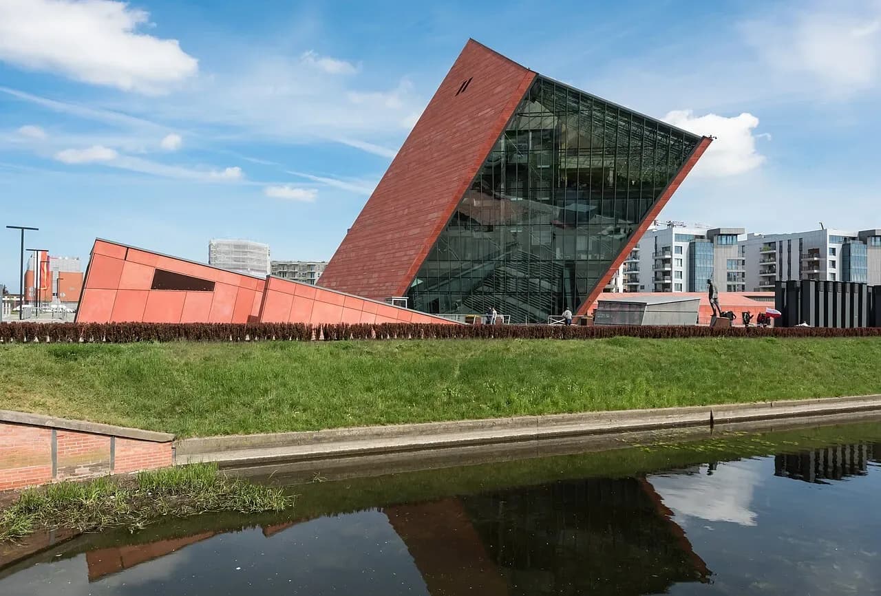 The Museum of the Second World War in Gdańsk, a tilted red and glass tower beside a canal | BudgetBro