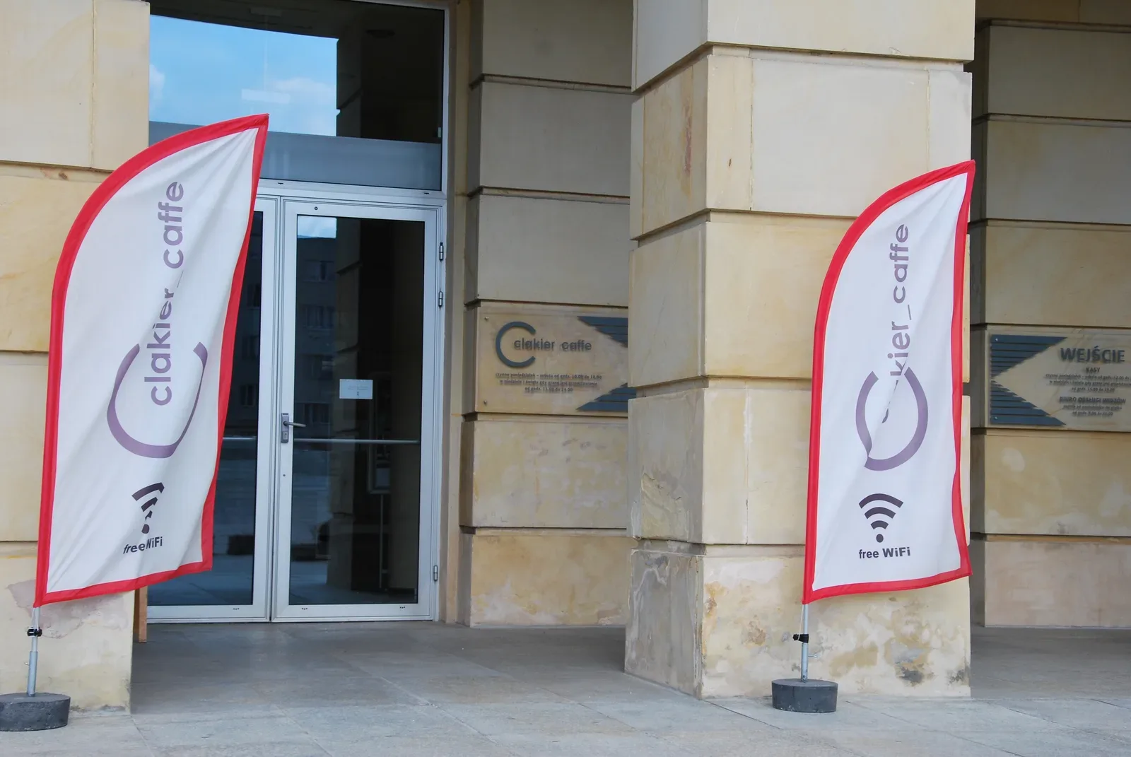 Two cafe flags with a free wifi symbol outside a stone building entrance | BudgetBro