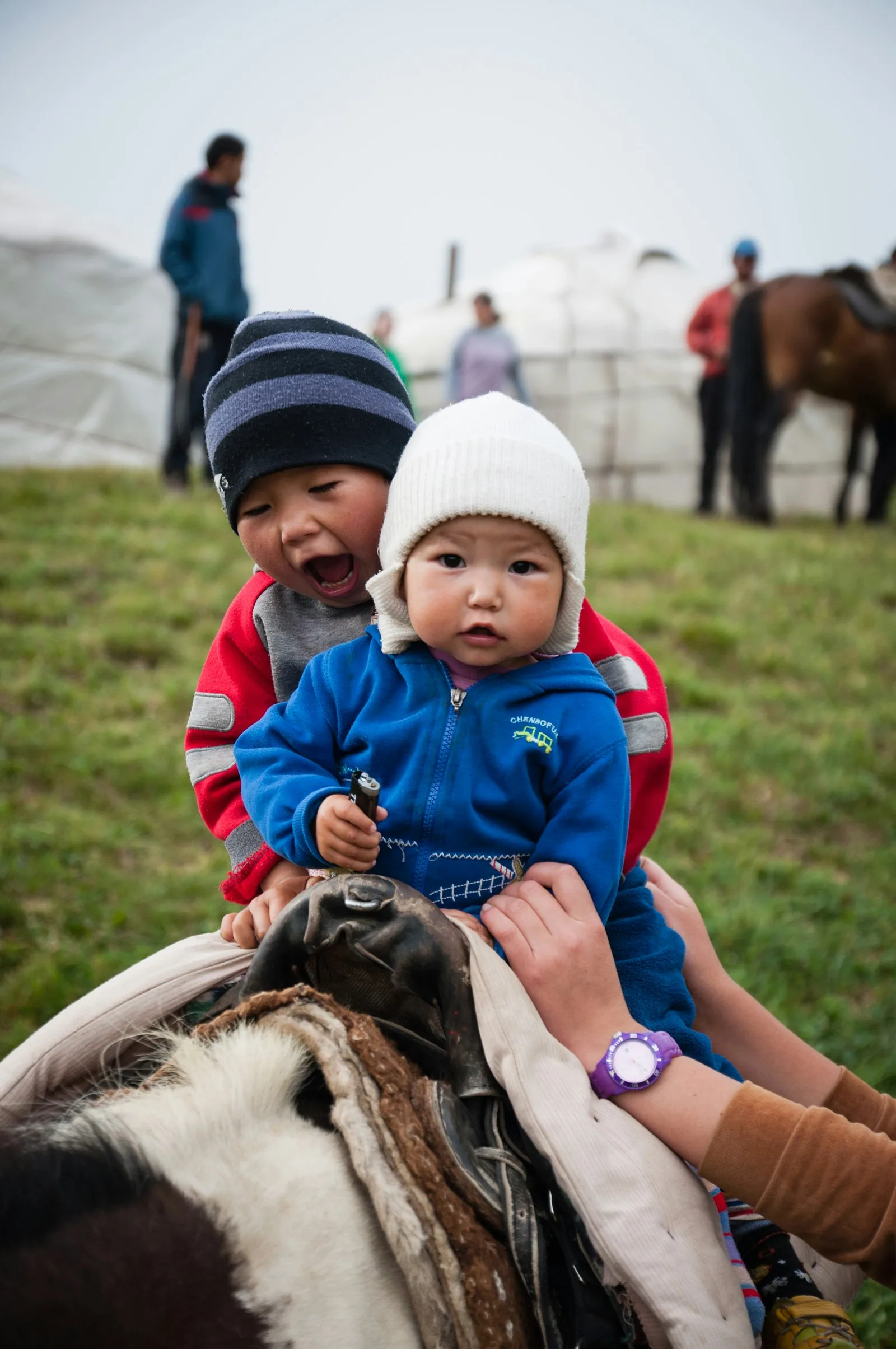 Two young Kyrgyz children in warm hats sitting on a horse at a yurt camp during a nomad festival | BudgetBro